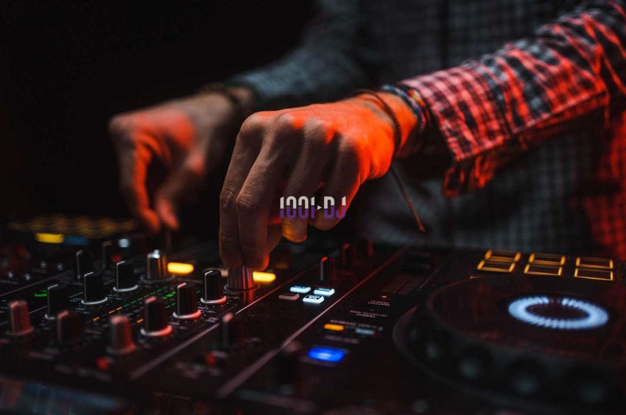 Main ajustant des commandes sur une table de mixage DJ illuminée par des lumières rouges et oranges.