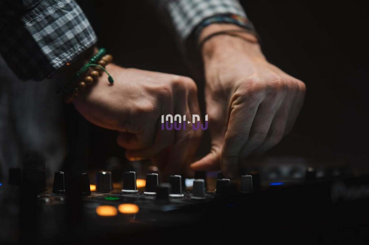 Mains ajustant des commandes sur une table de mixage audio dans un environnement faiblement éclairé.