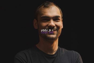 Portrait d'un homme souriant avec un éclairage tamisé sur fond sombre, un logo ’1001 DJ’ superposé au centre.