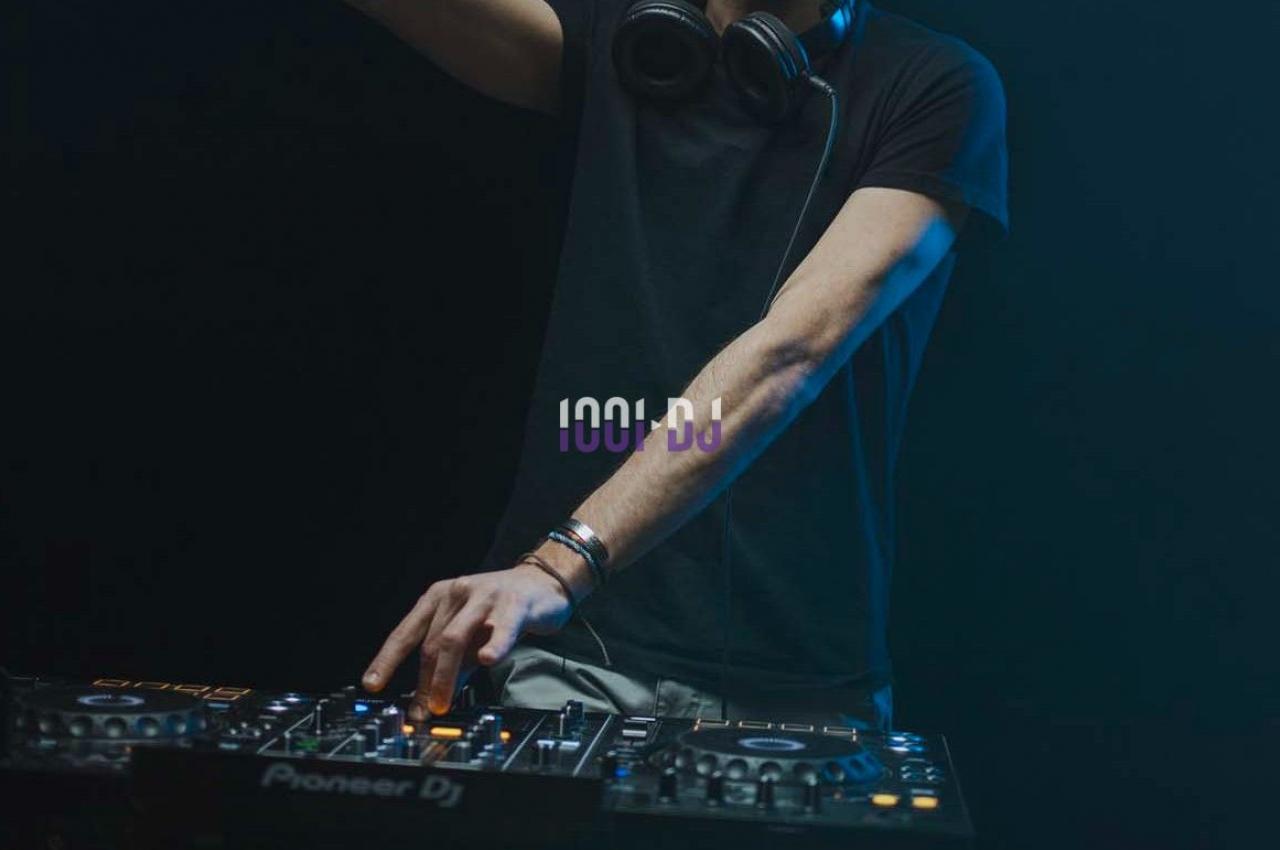 Un DJ mixant de la musique sur une table de mixage dans une ambiance sombre avec des éclairages tamisés.