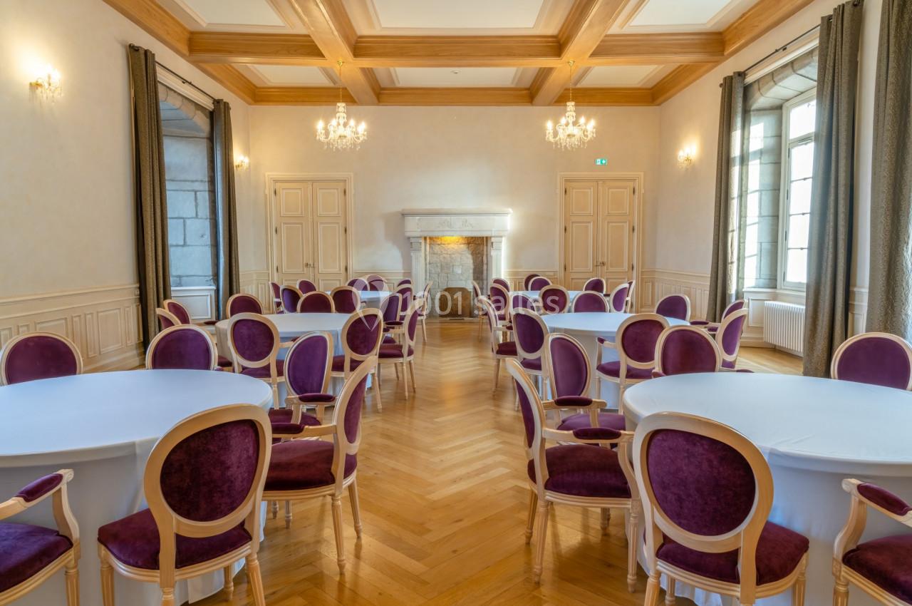 Salle élégante avec parquet, tables rondes couvertes de nappes blanches et chaises violettes, éclairée par des lustres.