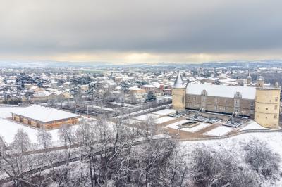 Vue aérienne d'un château entouré de neige, avec une petite ville et un paysage hivernal en arrière-plan.