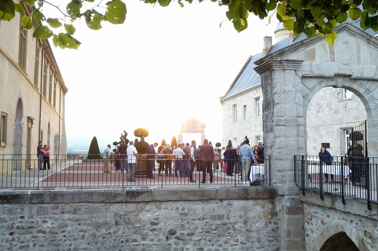 Groupe de personnes rassemblées sur une terrasse en pierre au coucher du soleil, près d'un bâtiment historique.
