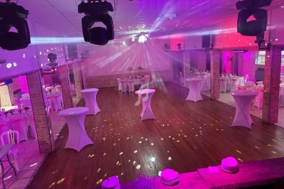Salle de réception décorée avec des tables dressées, des drapés suspendus et un éclairage coloré.