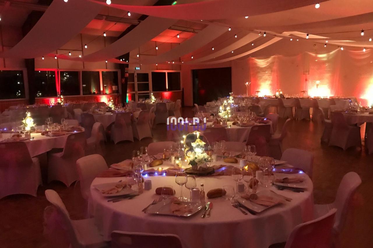 Salle de réception décorée avec des tables rondes dressées, éclairage tamisé et guirlandes lumineuses suspendues.