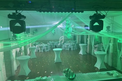 Salle de réception décorée avec des tables dressées, des drapés suspendus et un éclairage coloré.