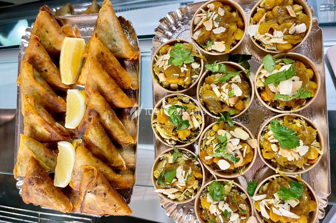 Assortiment de samoussas dorés avec des quartiers de citron et petits bols garnis de fruits secs et herbes fraîches.