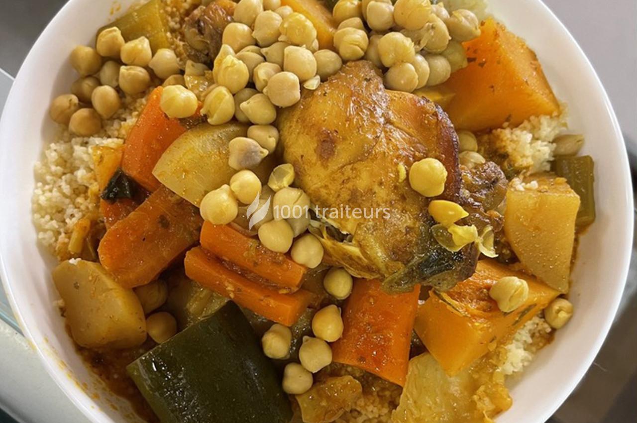 Plat de couscous garni de légumes variés, pois chiches et morceaux de viande dans un bol blanc.
