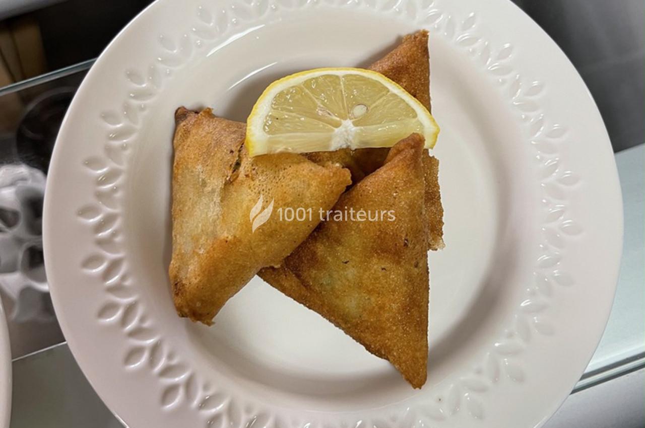 Trois samoussas dorés servis dans une assiette blanche avec une tranche de citron.