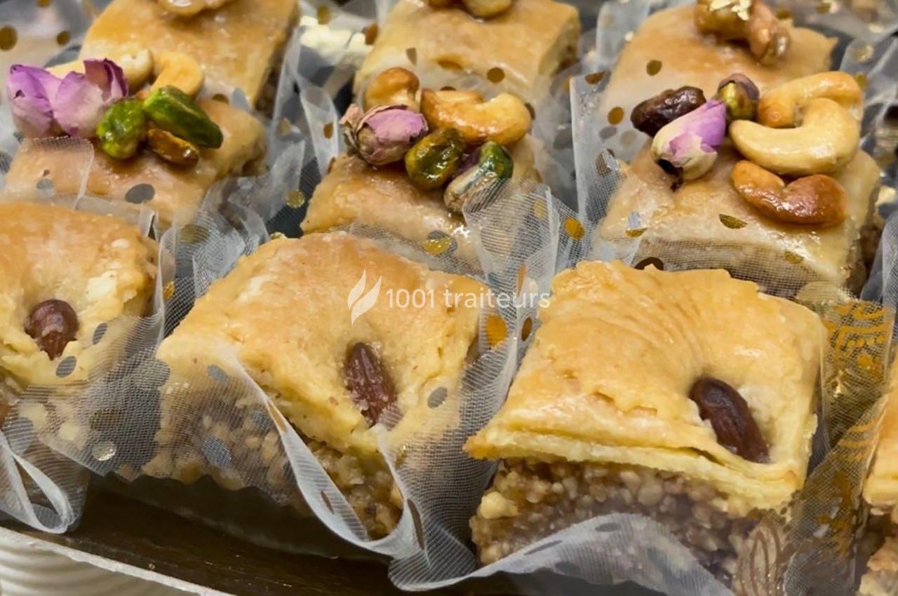 Assortiment de baklavas garnis de noix, pistaches et décorés de fleurs séchées, présentés dans des caissettes.
