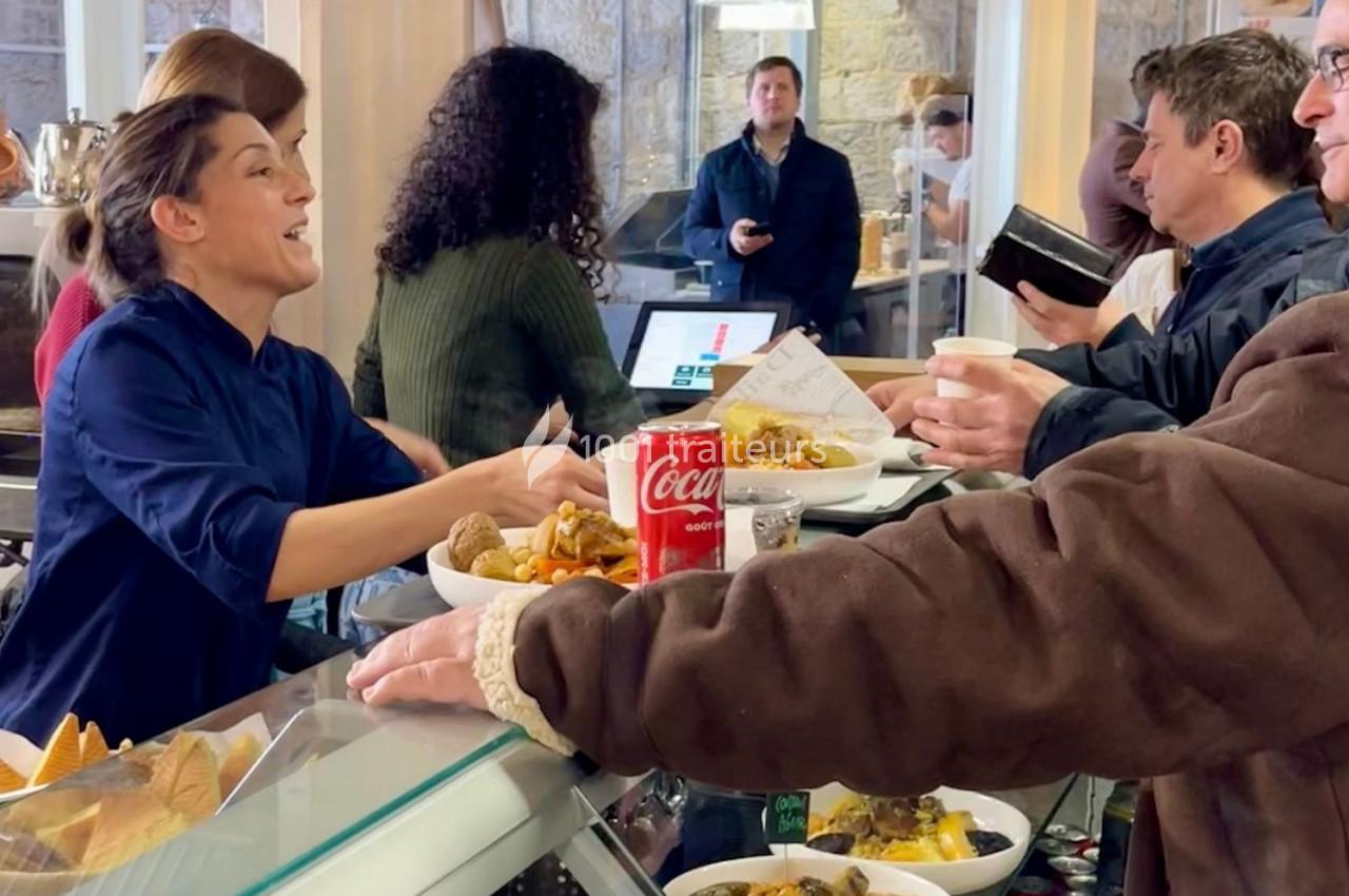 Une employée sert des clients à un comptoir de restaurant, avec des plats et une canette de soda visibles.