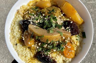 Assiette de couscous garnie de légumes, fruits secs, viande et herbes fraîches, servie sur une table en extérieur.