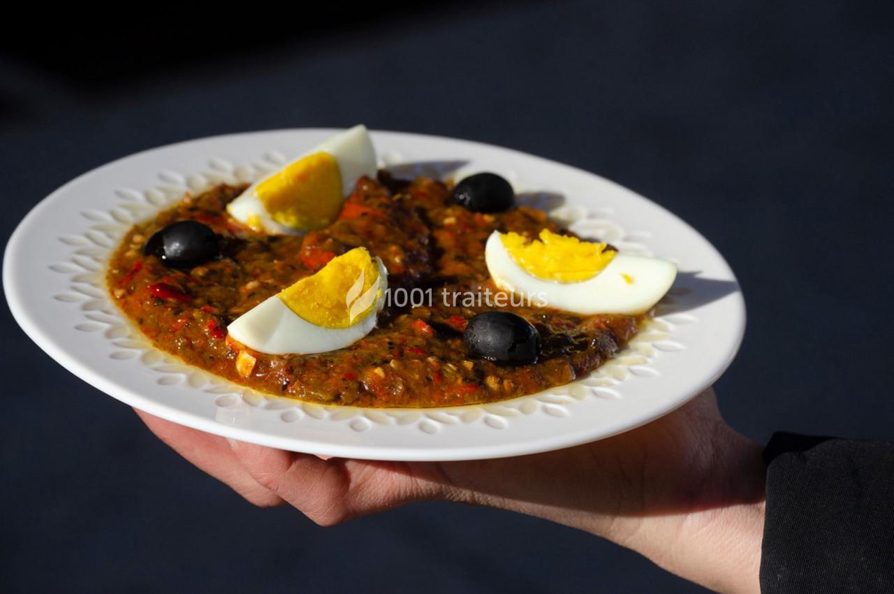 Assiette de salade méchouia garnie d'œufs durs et d'olives noires, tenue à la main.