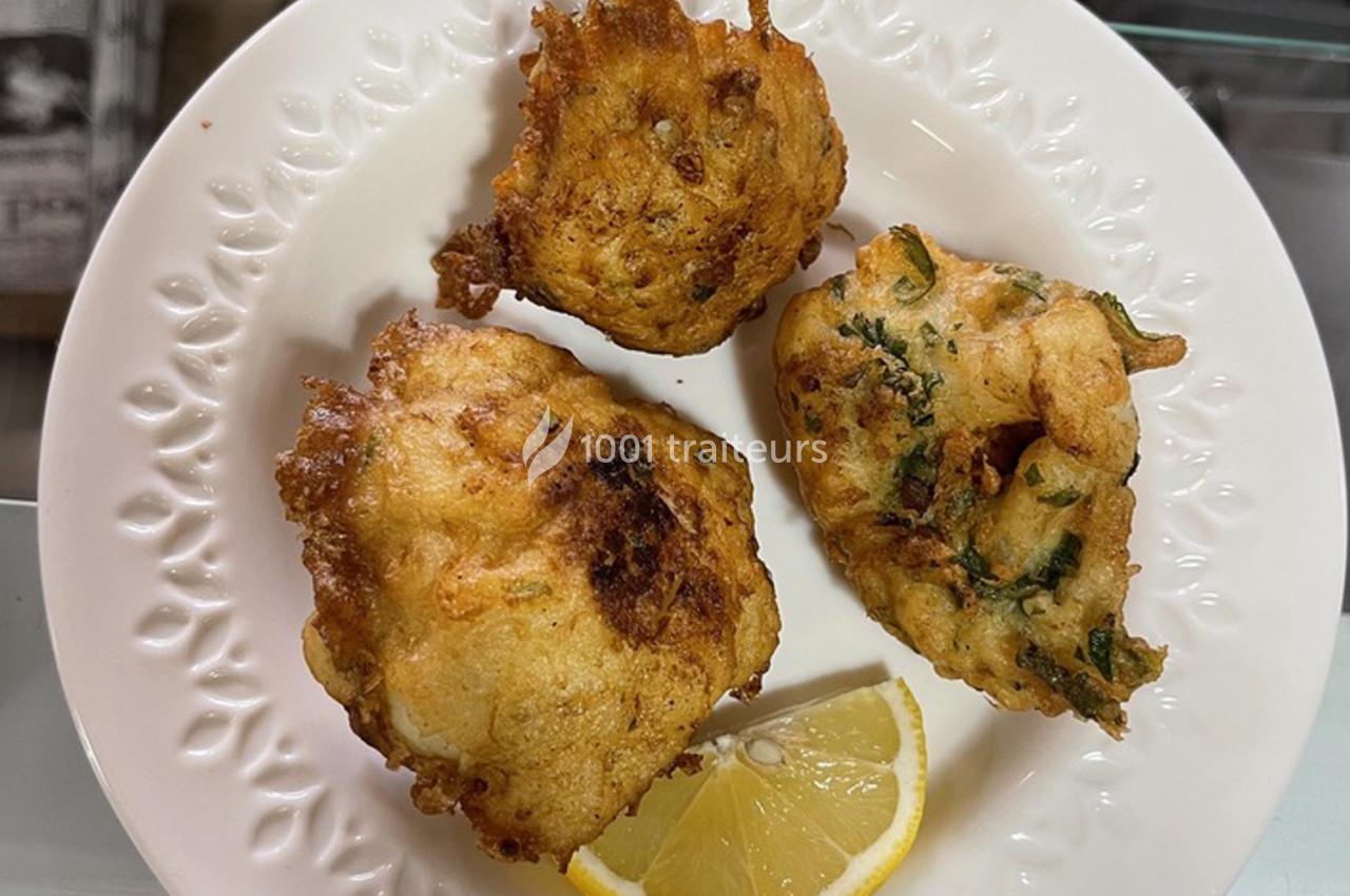 Beignets dorés sur une assiette blanche, accompagnés d'un quartier de citron.