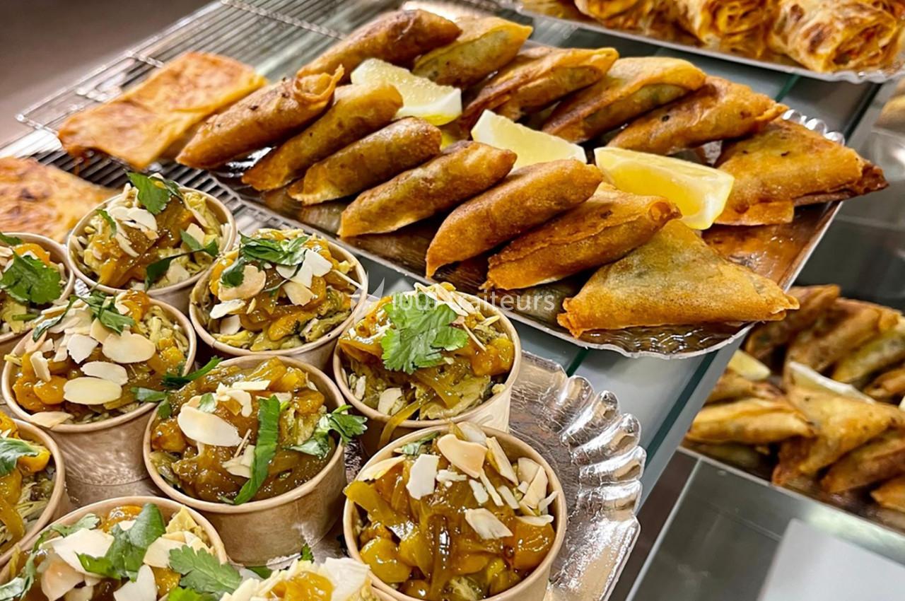 Assortiment de samoussas dorés, crêpes farcies et verrines garnies de légumes et amandes, décorées de coriandre.