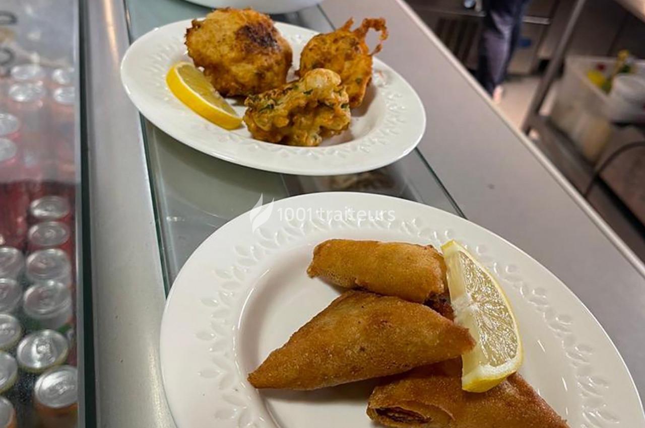 Assiette contenant des samoussas dorés avec un quartier de citron, posée sur un comptoir près d'une autre assiette de…