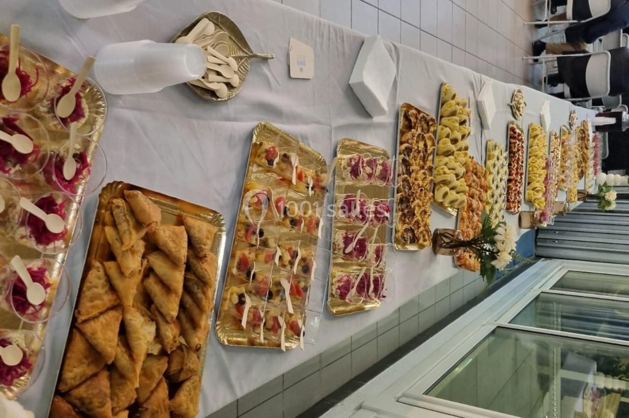 Buffet composé de divers plats salés et sucrés présentés sur des plateaux dorés disposés sur une longue table blanche.