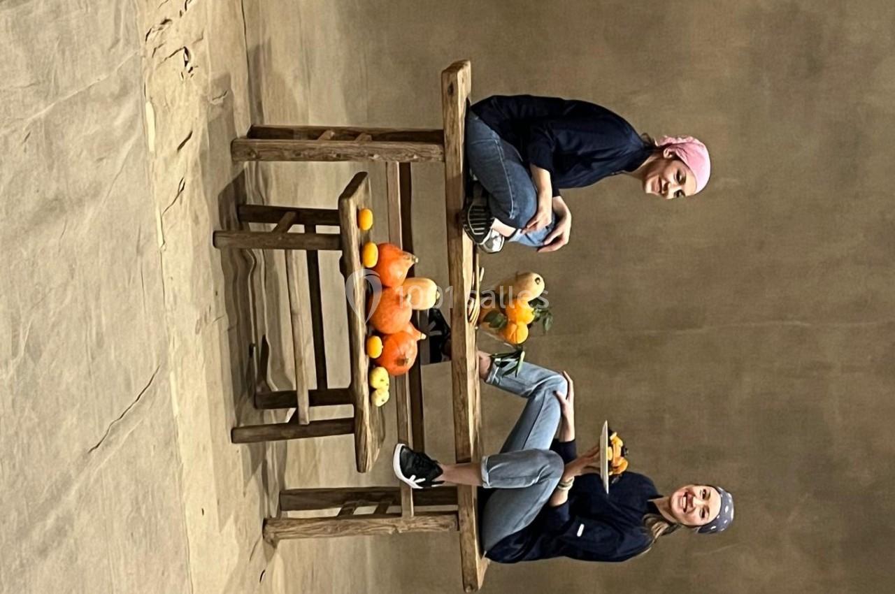 Deux personnes assises à une table en bois avec des courges et des fruits disposés autour.