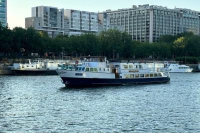 Pont supérieur d'un bateau aménagé avec des tables hautes et des chaises, amarré près d'une rive sous un ciel dégagé.