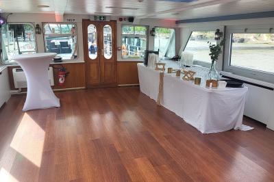 Pont supérieur d'un bateau aménagé avec des tables hautes et des chaises, amarré près d'une rive sous un ciel dégagé.