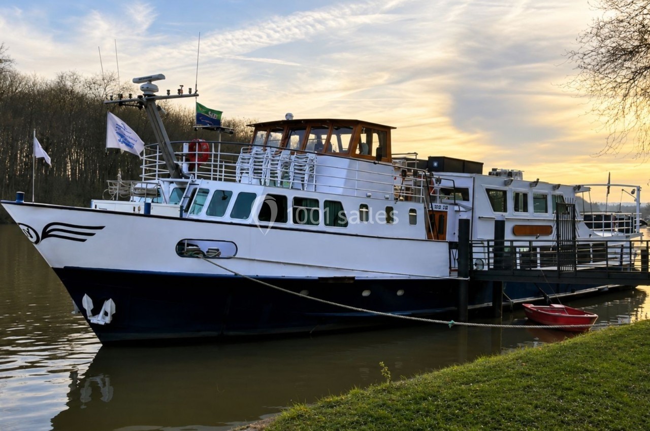 Bateau amarré à un ponton sur une rivière, entouré d'arbres et éclairé par une lumière de fin de journée.