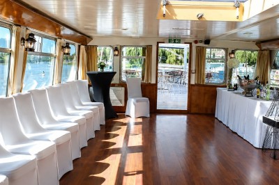 Un capitaine en uniforme utilise une radio dans la cabine d'un bateau, avec vue sur une rivière bordée d'arbres.