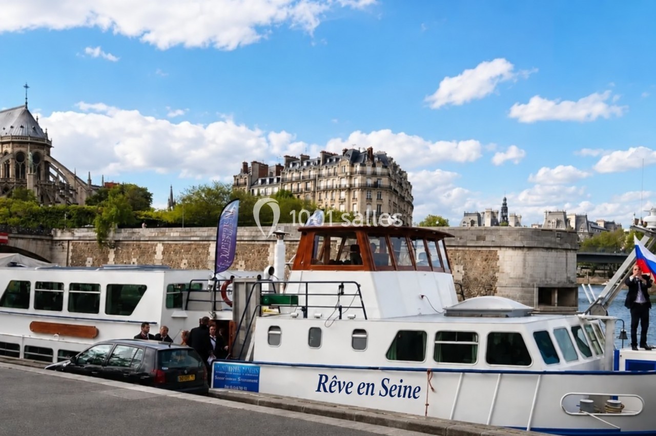 Bateau de croisière amarré sur la Seine à Paris, avec des passagers montant à bord et des bâtiments en arrière-plan.