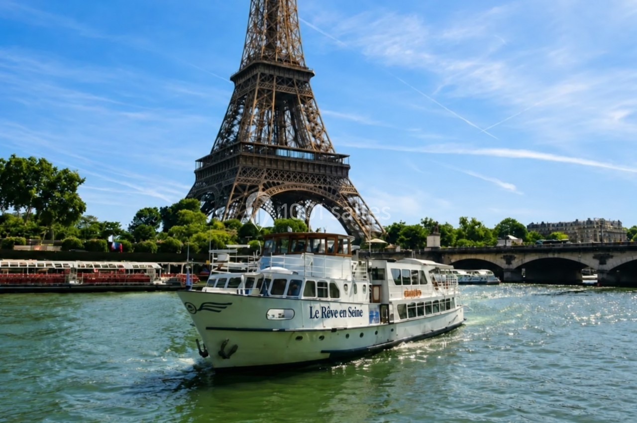 Bateau de croisière naviguant sur la Seine devant la tour Eiffel par une journée ensoleillée.