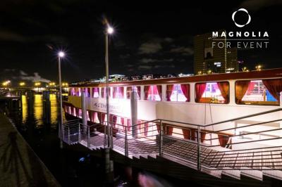 Salle de réception sur une péniche avec tables rondes dressées, rideaux rouges et buffet de desserts au premier plan.