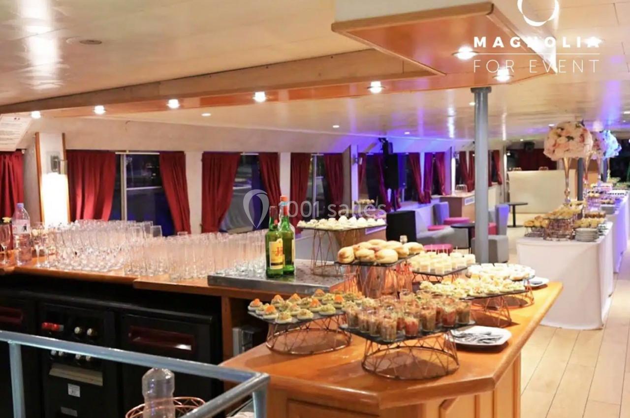 Buffet élégant avec verrines, pains garnis et boissons, disposé dans une salle lumineuse avec rideaux rouges.