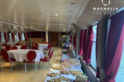Salle de réception sur une péniche avec tables rondes dressées, rideaux rouges et buffet de desserts au premier plan.