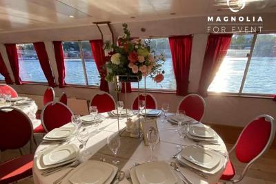 Salle de réception sur une péniche avec tables rondes dressées, rideaux rouges et buffet de desserts au premier plan.