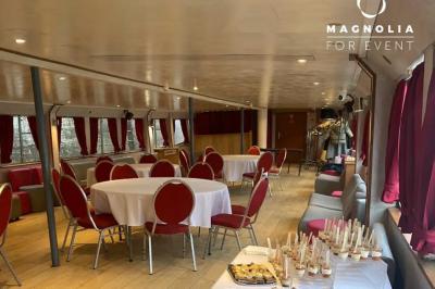 Salle de réception sur une péniche avec tables rondes dressées, rideaux rouges et buffet de desserts au premier plan.