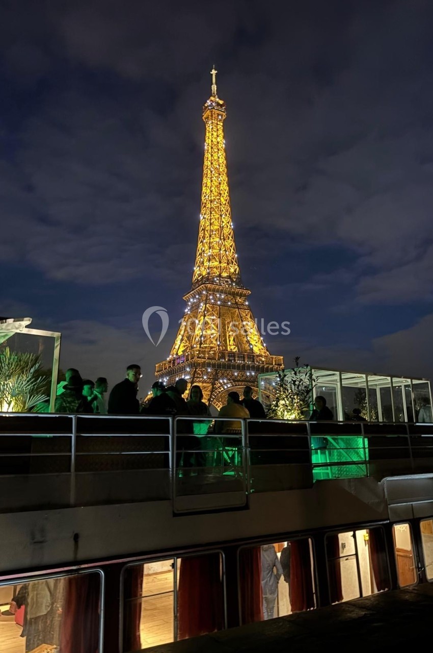 Vue nocturne de la tour Eiffel illuminée, prise depuis un bateau avec des passagers sur le pont.