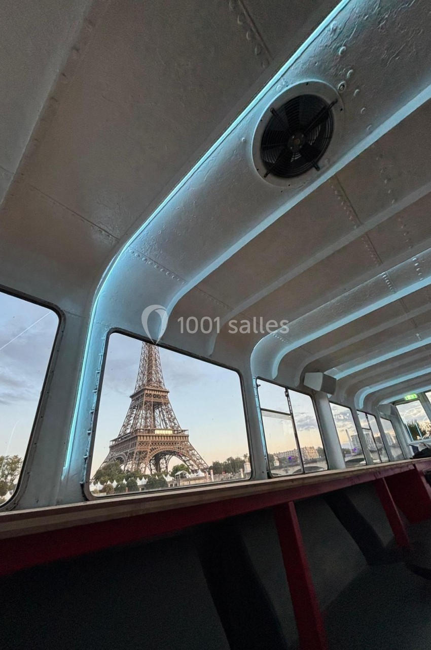 Vue de la tour Eiffel depuis l'intérieur d'un bateau avec des fenêtres encadrant le monument au crépuscule.