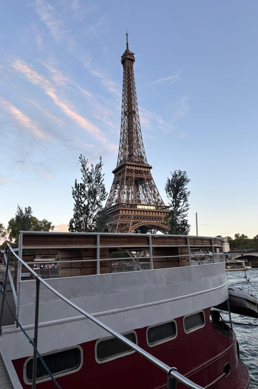 Vue de la Tour Eiffel au crépuscule depuis un quai, avec une péniche rouge et blanche au premier plan.