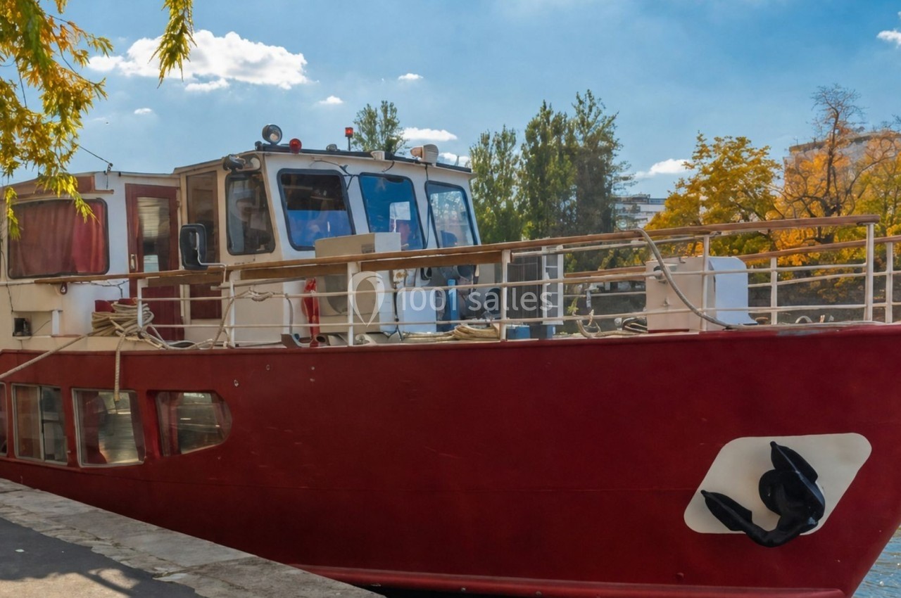Bateau rouge amarré au bord d'une rivière, entouré d'arbres aux couleurs automnales.