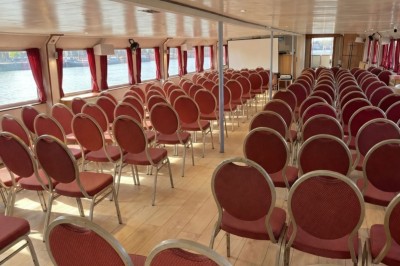 Intérieur d'une salle spacieuse avec parquet, canapés colorés, tables rondes noires et rideaux rouges.