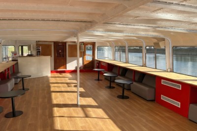 Intérieur d'une salle spacieuse avec parquet, canapés colorés, tables rondes noires et rideaux rouges.