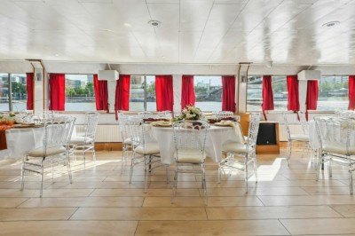 Intérieur d'une salle spacieuse avec parquet, canapés colorés, tables rondes noires et rideaux rouges.