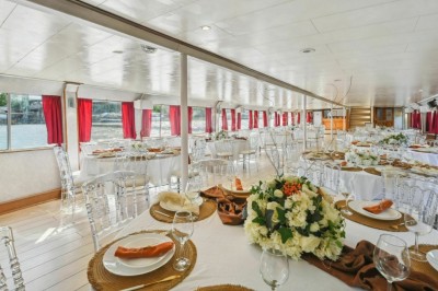 Intérieur d'une salle spacieuse avec parquet, canapés colorés, tables rondes noires et rideaux rouges.