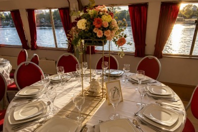 Intérieur d'une salle spacieuse avec parquet, canapés colorés, tables rondes noires et rideaux rouges.