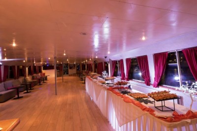 Intérieur d'une salle spacieuse avec parquet, canapés colorés, tables rondes noires et rideaux rouges.