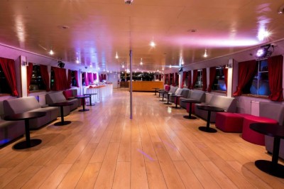 Intérieur d'une salle spacieuse avec parquet, canapés colorés, tables rondes noires et rideaux rouges.