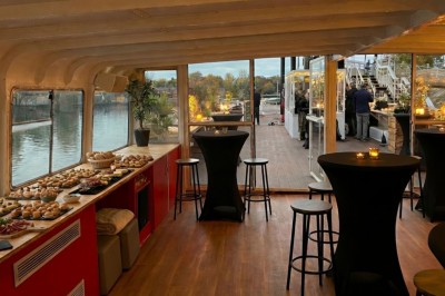 Intérieur d'une salle spacieuse avec parquet, canapés colorés, tables rondes noires et rideaux rouges.