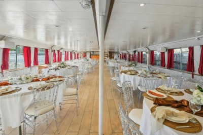 Intérieur d'une salle spacieuse avec parquet, canapés colorés, tables rondes noires et rideaux rouges.