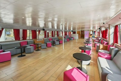 Intérieur d'une salle spacieuse avec parquet, canapés colorés, tables rondes noires et rideaux rouges.