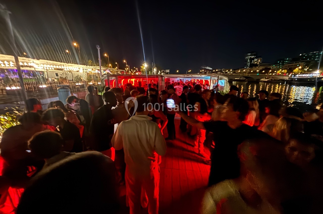 Personnes rassemblées de nuit sur un quai illuminé, avec une ambiance festive et des lumières rouges.