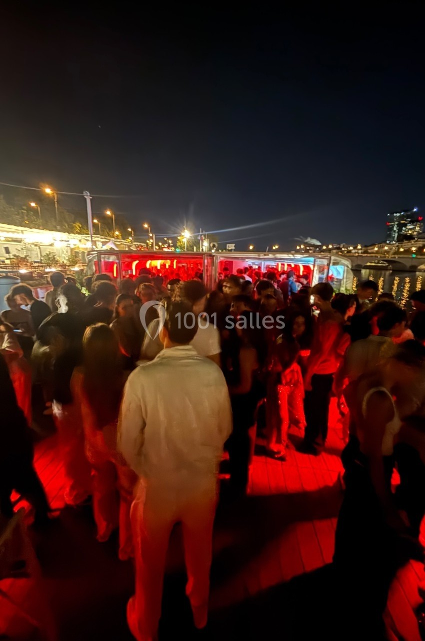 Groupe de personnes rassemblées sur une terrasse extérieure éclairée par des lumières rouges, de nuit.