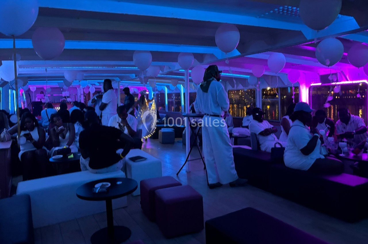 Personnes vêtues de blanc dans une salle éclairée par des lumières bleues et violettes, décorée de ballons blancs.